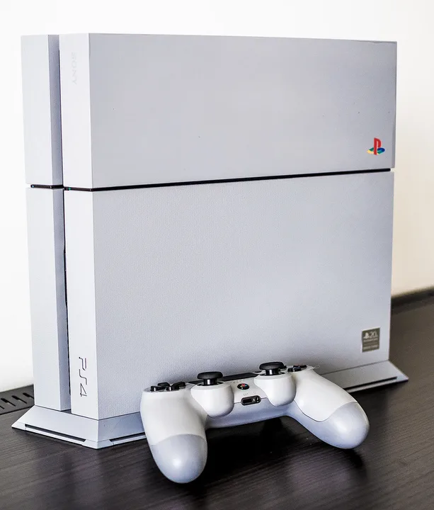 Original Grey PS4 20th Anniversary console upright beside its matching DualShock 4 controller