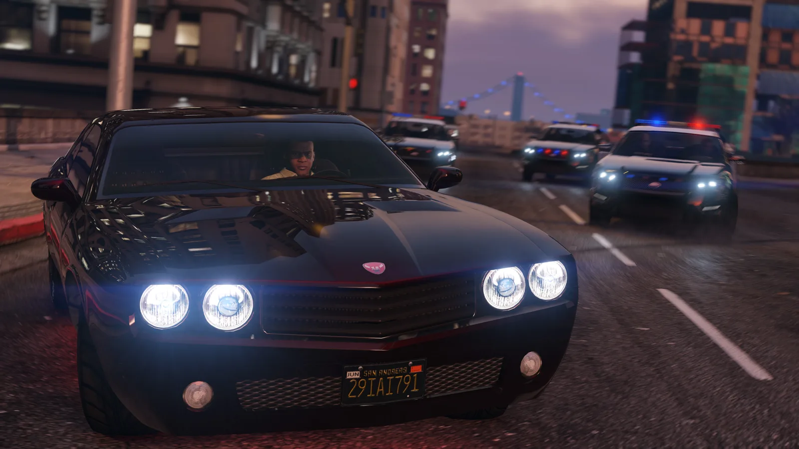 Official GTA V PC screenshot: Franklin driving a black car with police vehicles in pursuit.