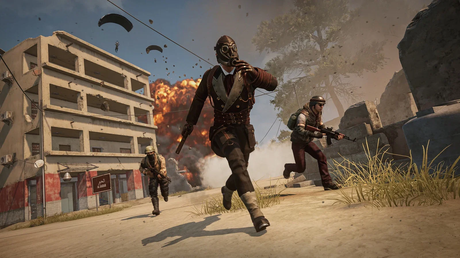 Armed players in tactical gear sprint past a pale apartment block as parachutes drift down and an explosion burns behind them