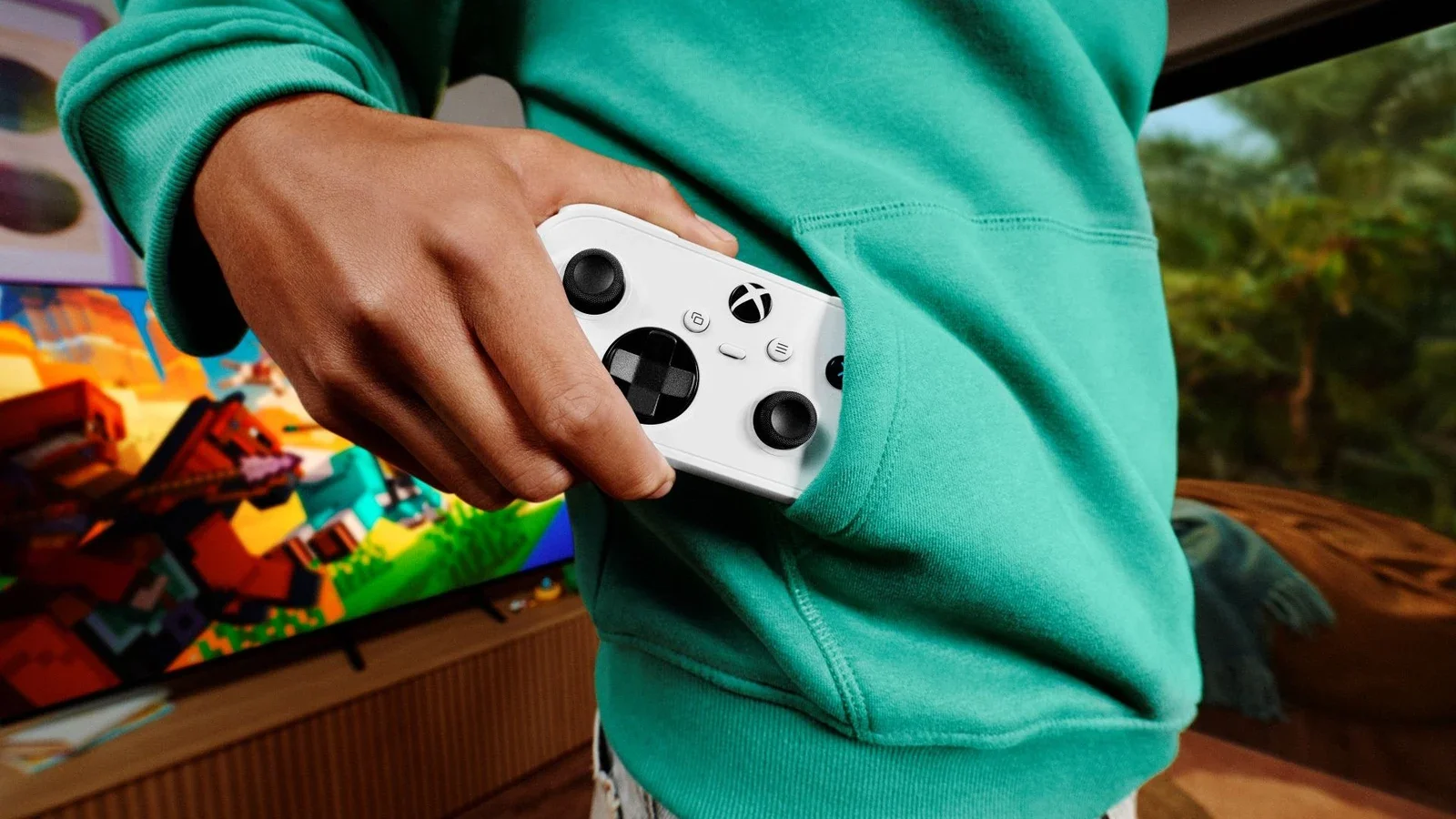 A person in a teal hoodie holding a white Xbox wireless controller