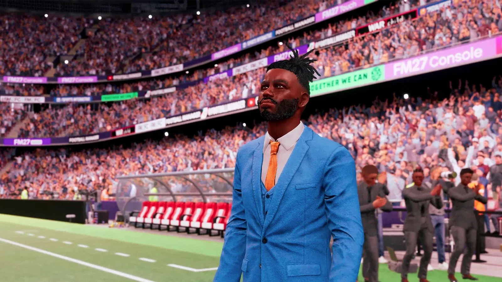 A manager in a bright blue suit and orange tie stands on the touchline of a crowded stadium, with staff celebrating behind him