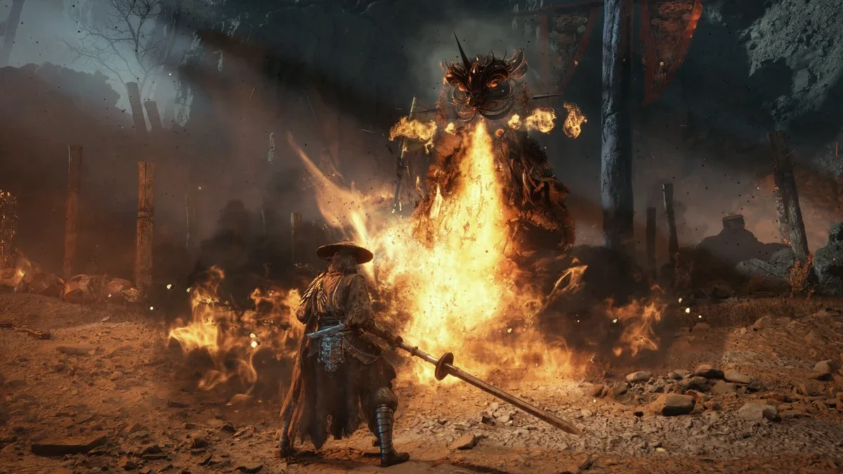 Soul, the swordsman in a wide straw hat, stands in a burning village as a towering flame-wreathed warrior lunges at him through fire and smoke